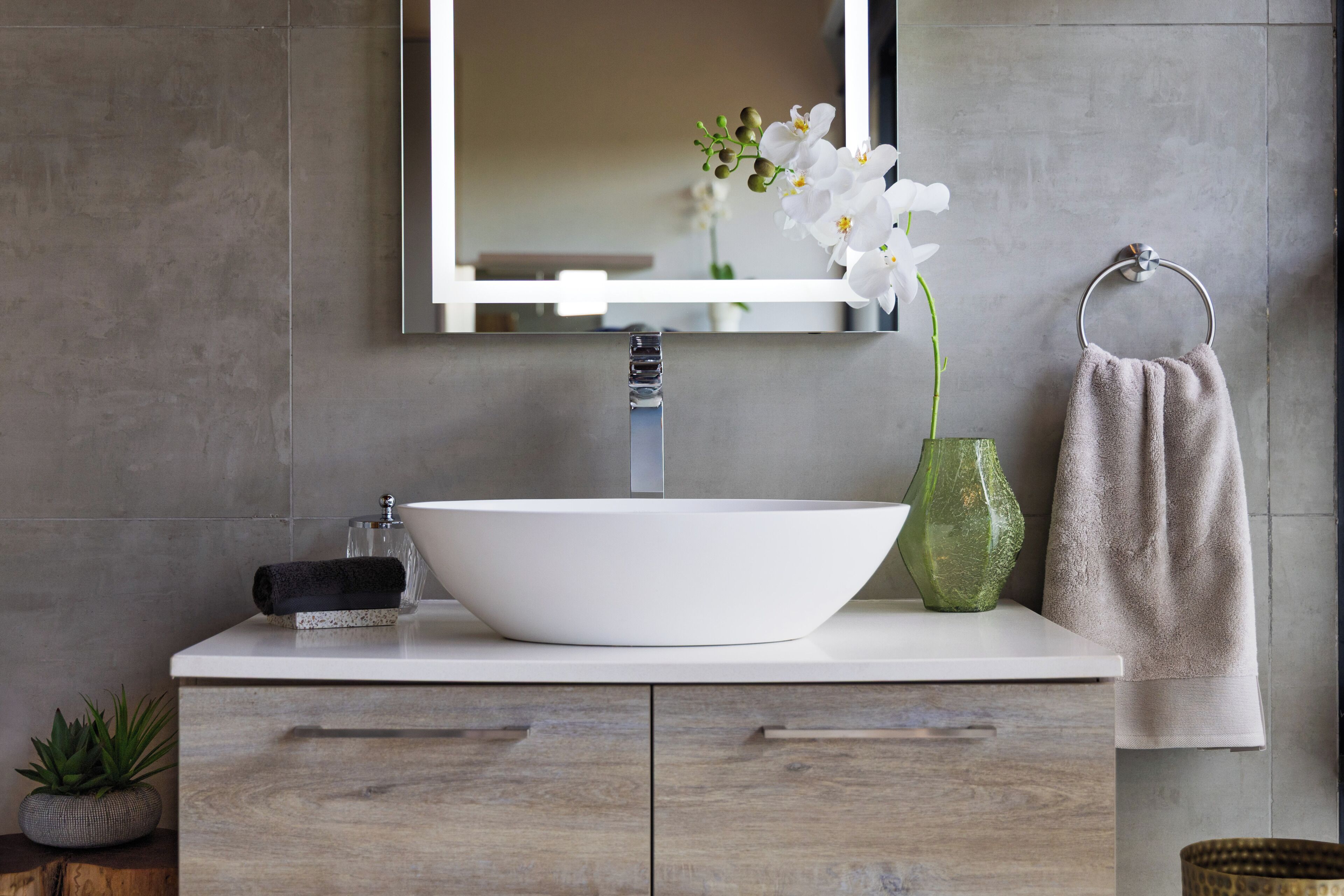 A bathroom with a white sink, a mirror, a towel ring, and a green vase with flowers.
