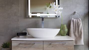 A bathroom with a white sink, a mirror, a towel ring, and a green vase with flowers.