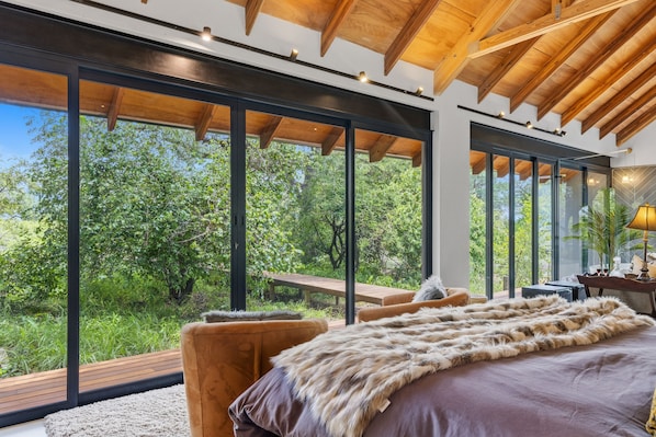 A bedroom with large windows, a wooden ceiling, and a fur throw on the bed.