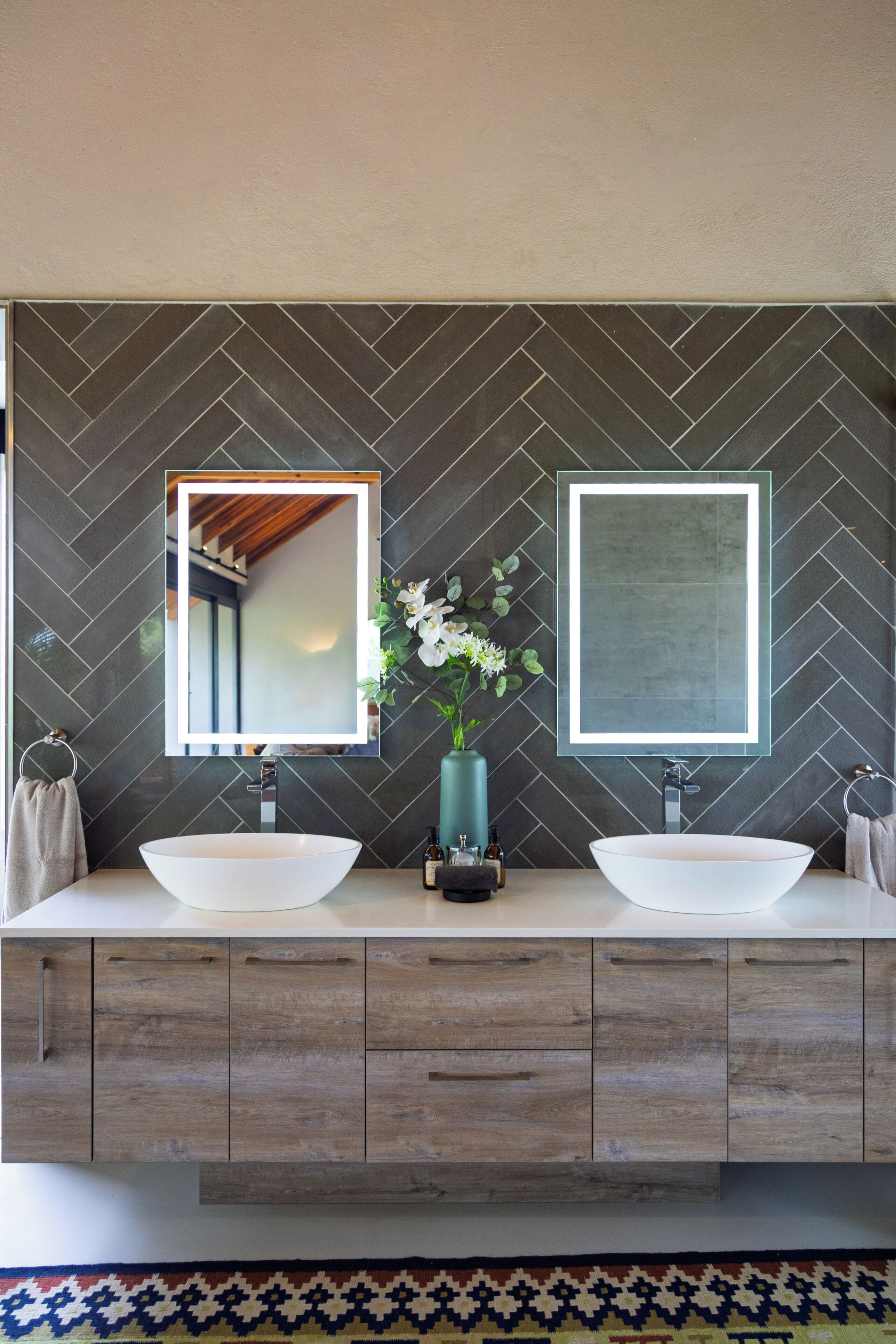 A bathroom with two sinks, a mirror, and a vase with flowers.