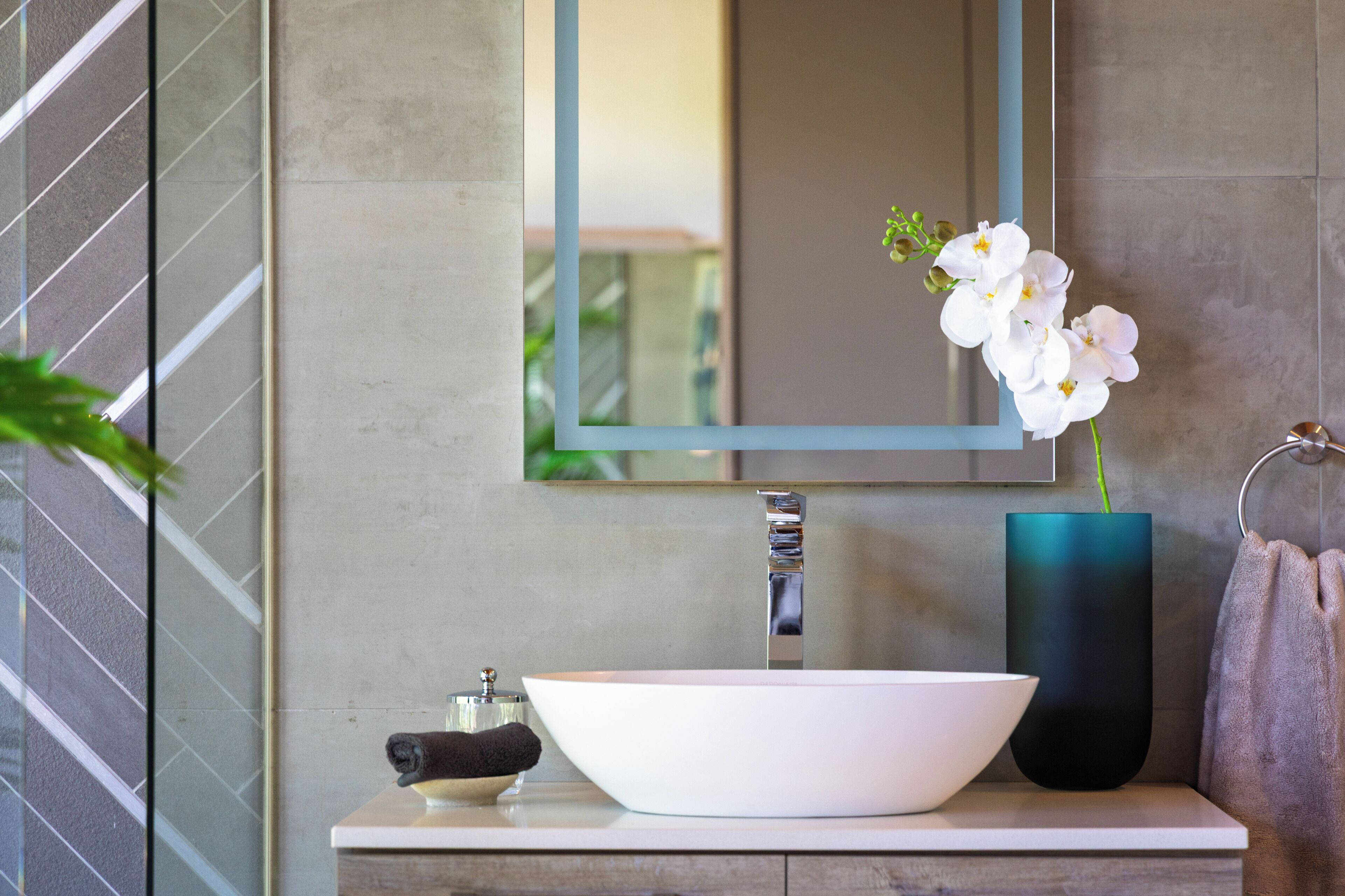 A bathroom with a white sink, a mirror, and a vase with white flowers.