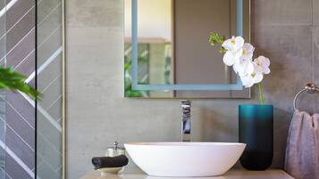 A bathroom with a white sink, a mirror, and a vase with white flowers.