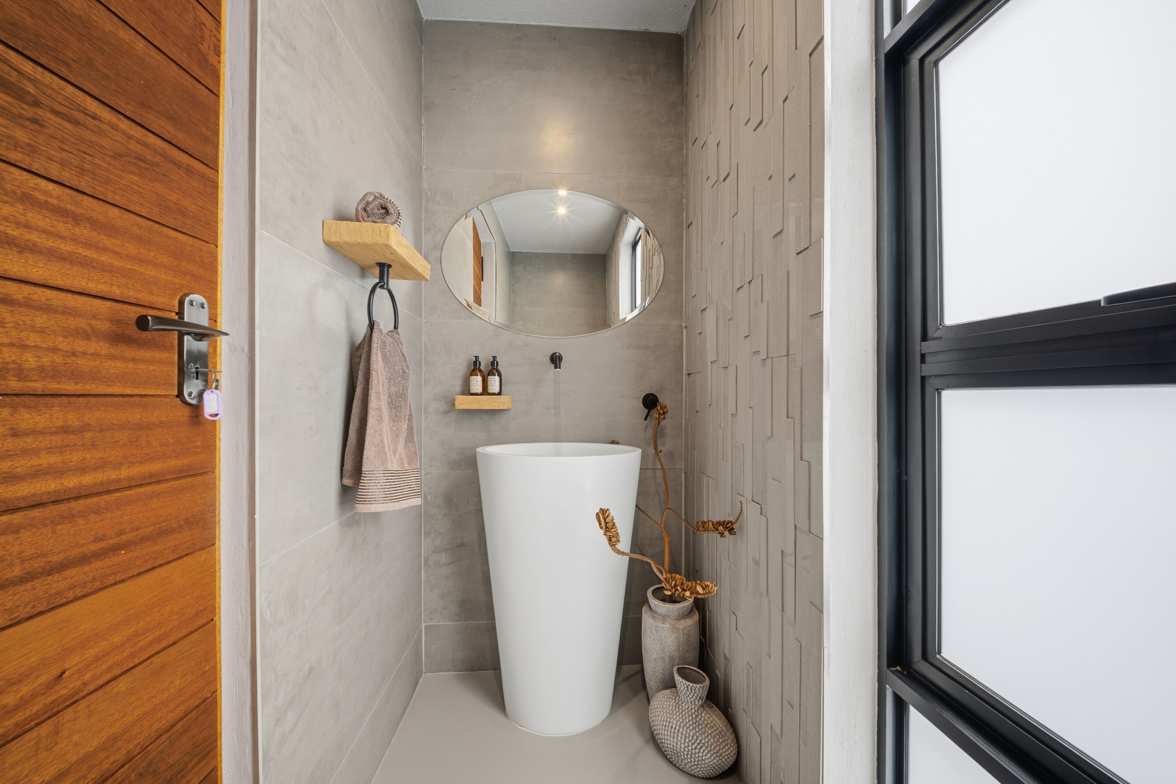 Ein Badezimmer mit Holztür, Waschbecken, Spiegel und Handtuchhalter.