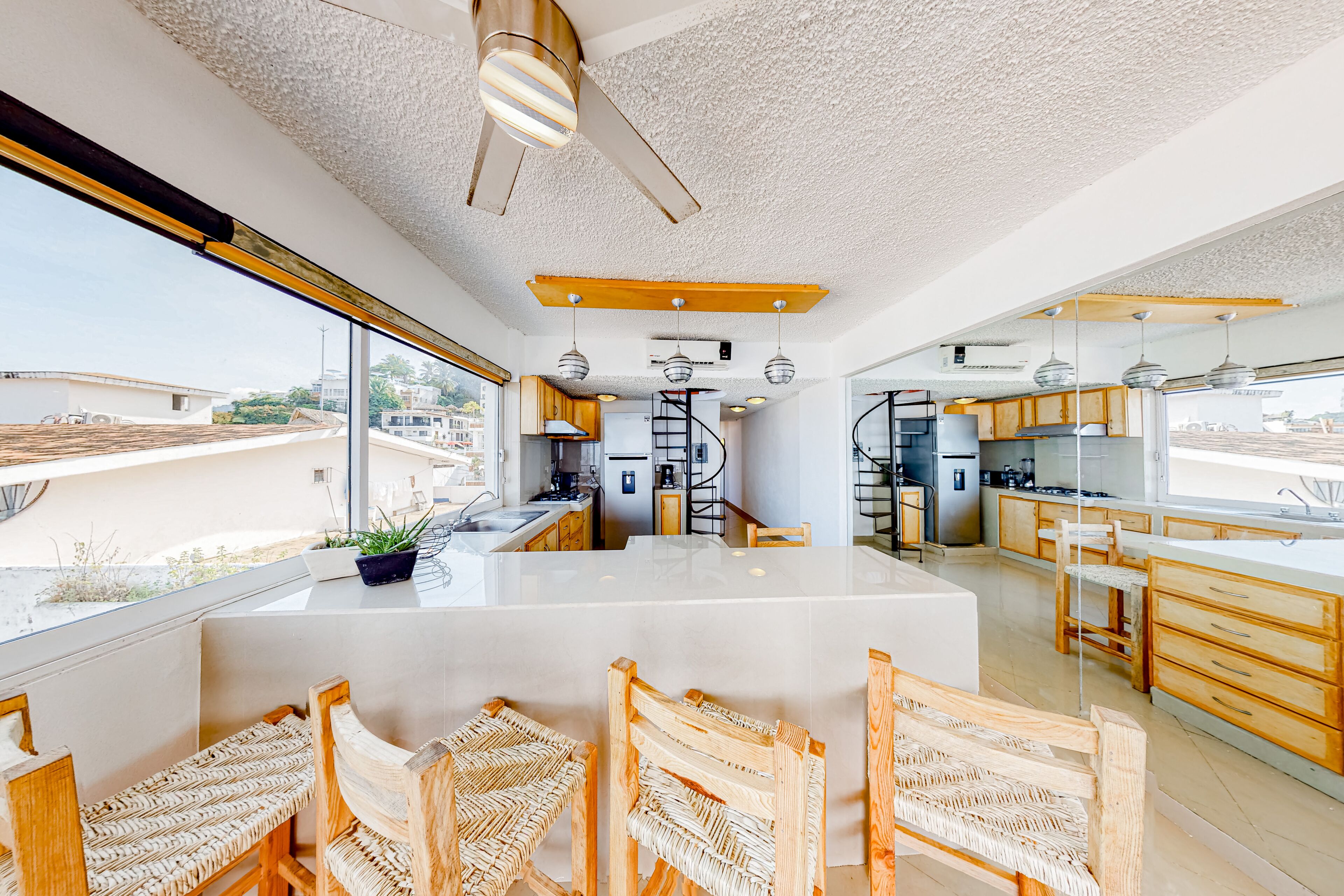 Cocina moderna con una isla central, sillas de madera y vistas de la ciudad a través de amplias ventanas.