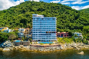 Un hôtel à plusieurs étages doté d’une piscine, entouré d’une végétation luxuriante et bordé d’une côte rocheuse.
