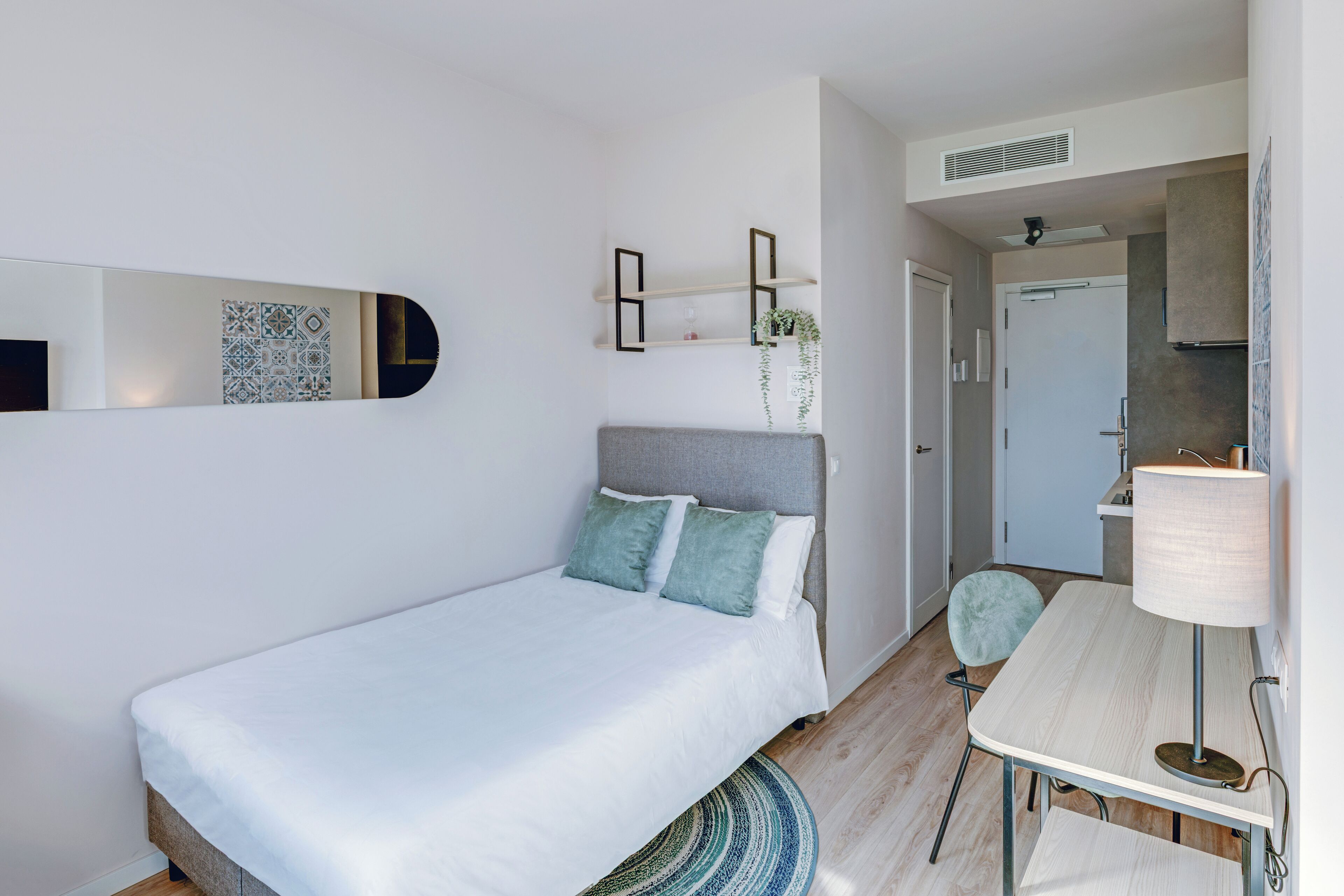 Un dormitorio con cama, escritorio, silla, espejo y una planta.