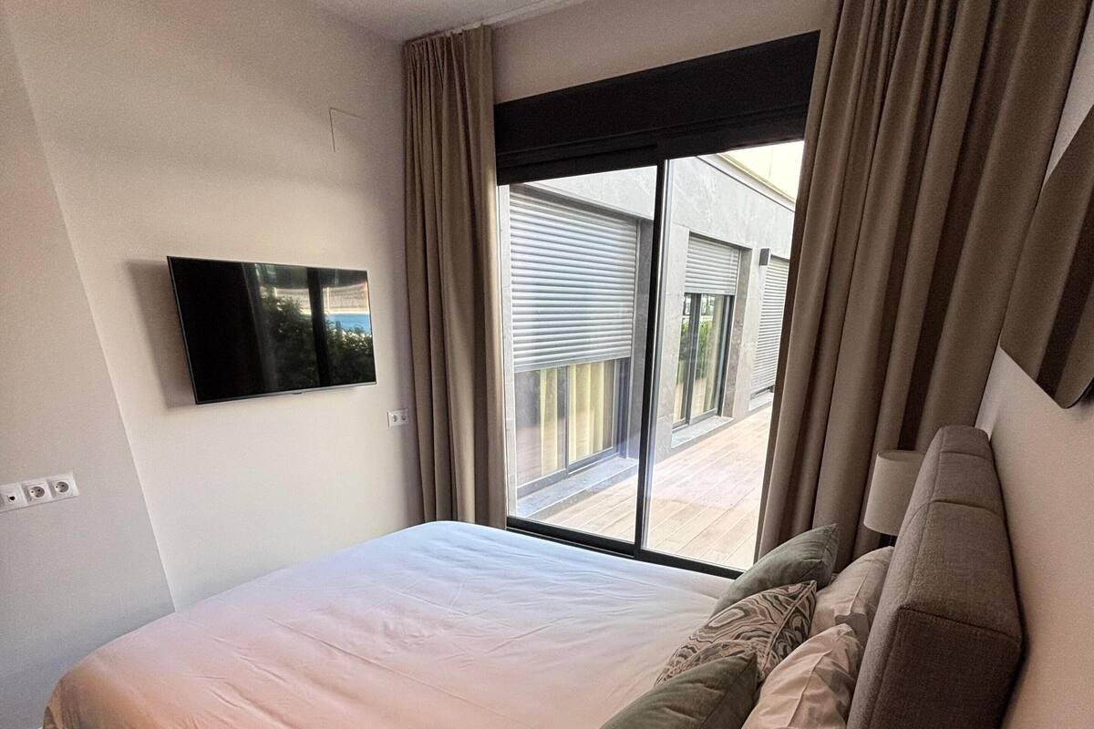 Ein Hotelzimmer mit einem großen Bett, einem an der Wand montierten Fernseher und Blick nach außen.