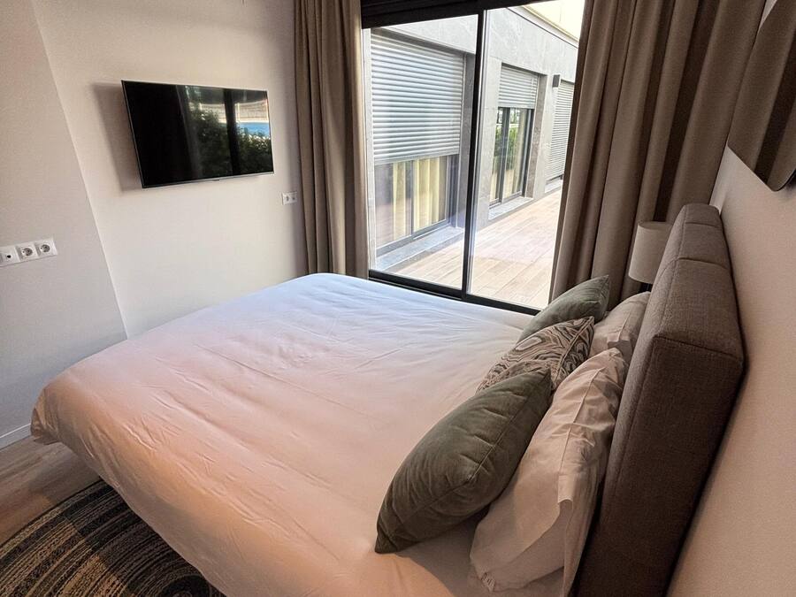 Ein Hotelzimmer mit einem großen Bett, einem an der Wand montierten Fernseher und Blick nach außen.