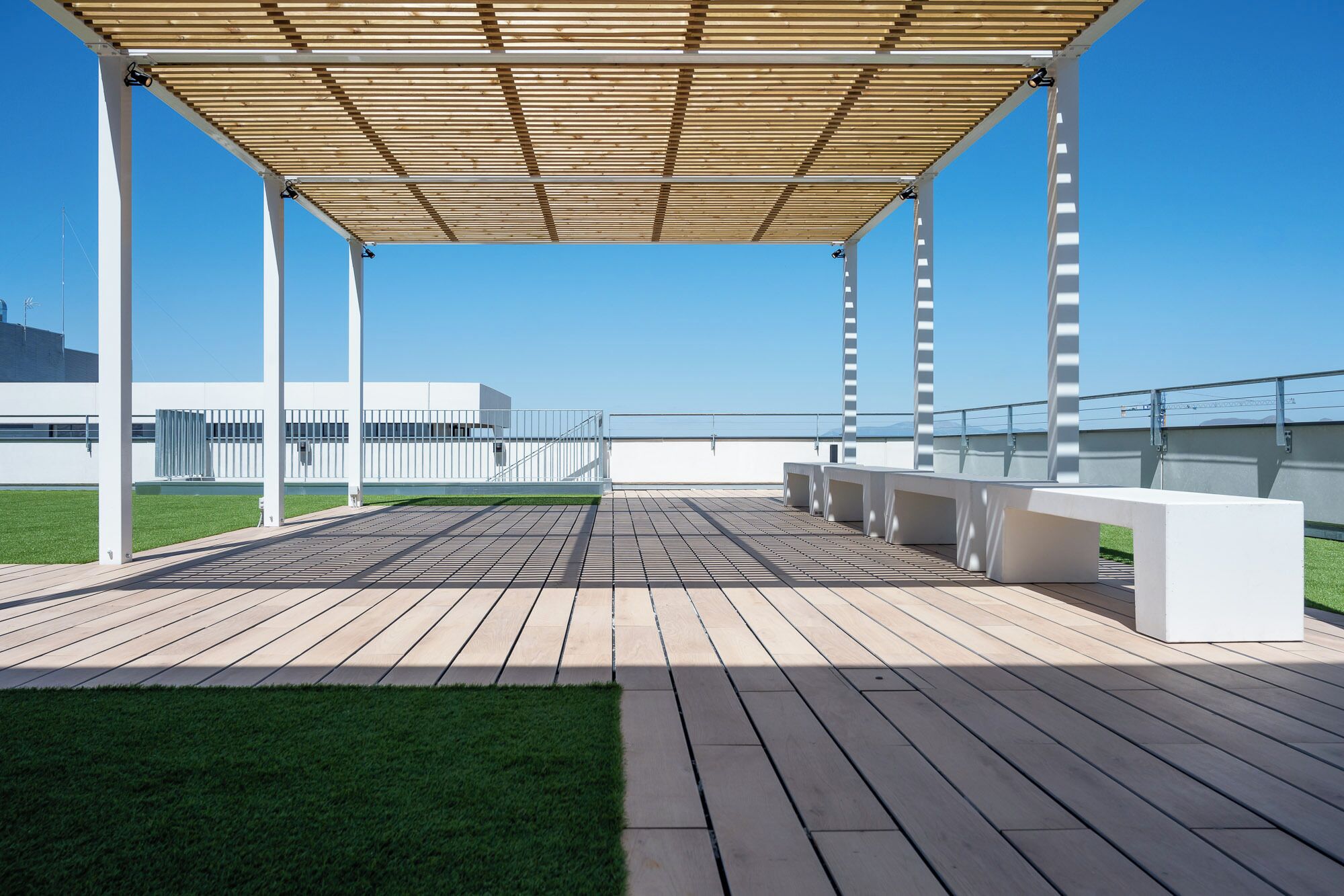 A covered outdoor area with a wooden deck, white columns, and a view of a modern building.