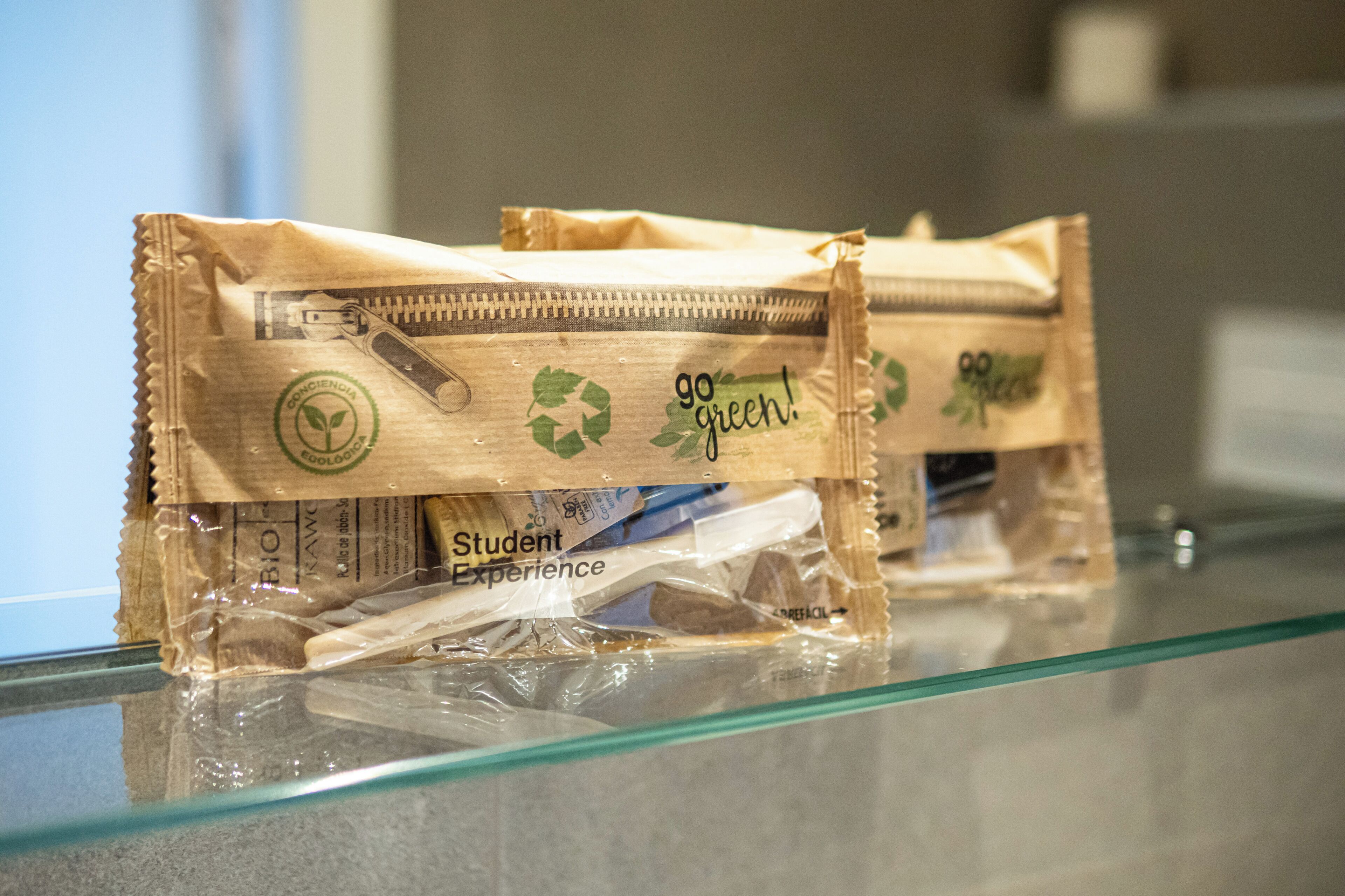 Two zippered bags with 'go green' and 'Student Experience' labels on a glass surface.