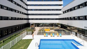 Un edificio moderno con un patio central, piscina y mobiliario exterior.