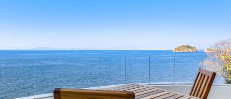 A wooden table and chair on a balcony with a clear view of the sea and a distant island.