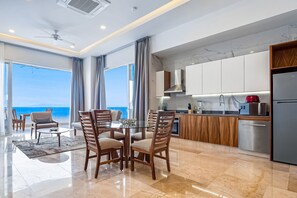Eine moderne Küche mit Meerblick, ein Essbereich mit rundem Tisch und ein Balkon mit Stühlen.