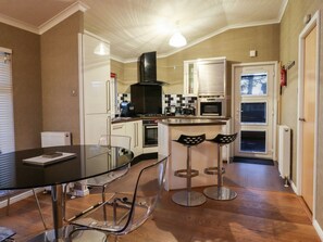 A modern kitchen with a glass dining table, stainless steel chairs, and a black range hood. - Washburn Lodge, Darley (Harrogate)