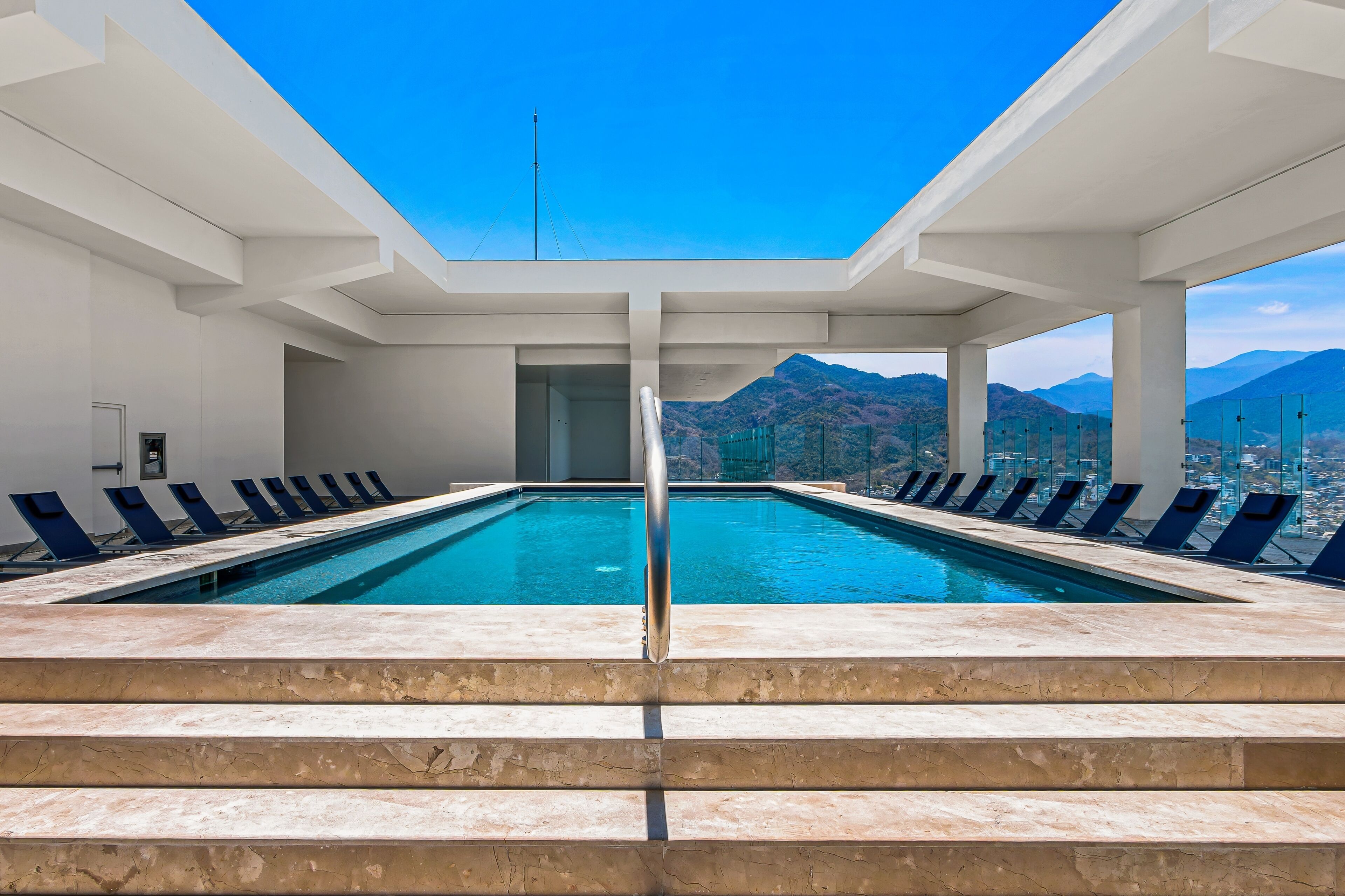 A swimming pool with steps leading up to it, surrounded by lounge chairs and a view of mountains.