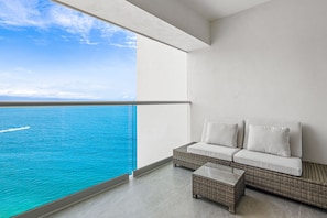 A balcony with a view of the ocean, a wicker sofa with white cushions, and a small table. - Oceanfront 1BR Puerto Vallarta condo w/ pool, gym (Puerto Vallarta)