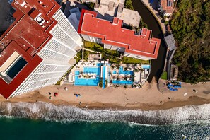 An aerial view of a coastal hotel with a red-roofed building, a pool area, and a beach. - Oceanfront 1BR Puerto Vallarta condo w/ pool, gym (Puerto Vallarta)