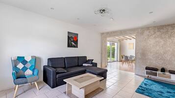 A modern living room with a sectional sofa, a patterned armchair, a coffee table, and a dining area visible through an open doorway.
