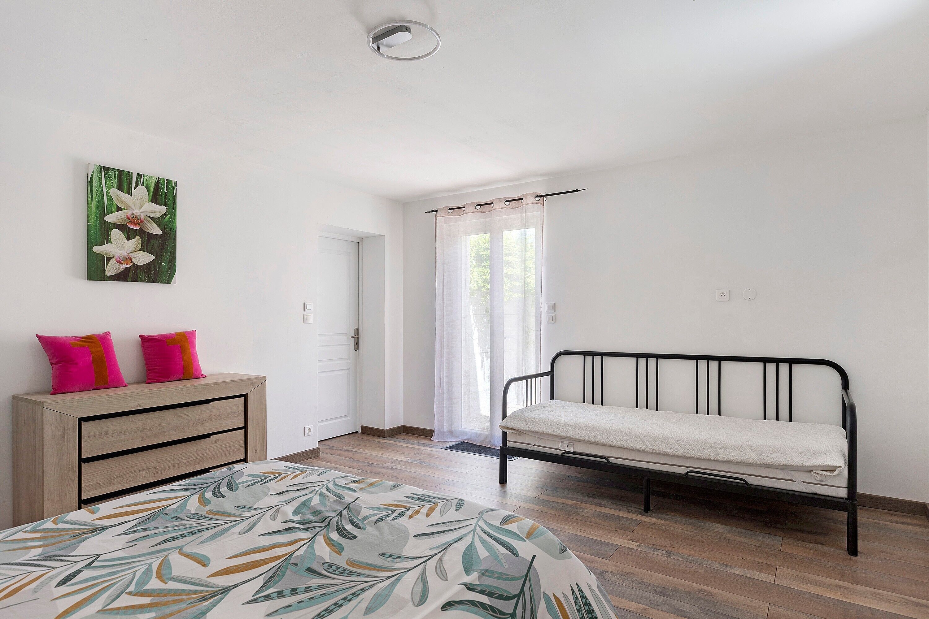 A bedroom with a bed, a dresser, a mirror, and a window with curtains.