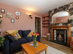 A cozy living room with a fireplace, a sofa, a coffee table with books, and a mirror above the fireplace.