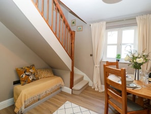 A bedroom with a bed, a wooden staircase, a dining area with a table and chairs, and a window with curtains.