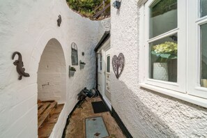 A narrow alleyway with a white wall, a wooden door, and a window with a flower pot.