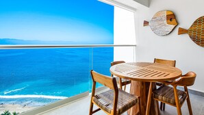 En balkon med udsigt over havet, et rundt træbord og to træstole.