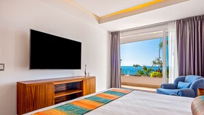 Ein Hotelzimmer mit einem großen Bett, einem Flachbildfernseher, einer Holztruhe zur Unterhaltung und einem Balkon mit Meerblick.