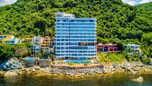 Ein mehrstöckiges Hotel mit Poolbereich, umgeben von üppiger Vegetation und einer felsigen Küste.