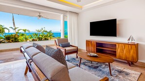 Ein modernes Wohnzimmer mit großem Fernseher, bequemen Sitzgelegenheiten und Blick auf den Ozean.