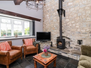 A cozy living room with stone walls, a fireplace, leather sofas, a flat-screen TV, and a wooden coffee table with a vase of flowers.