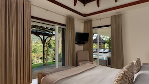 A hotel room with a bed, a TV, and a view of a pool and garden. - Peaceful 4-Bedroom Villa / Infinity Pool & Garden View (Bel Ombre)