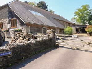 En byggnad av sten med ett sluttande tak, en trädörr och en skylt med texten ”Cowslip Barn”.
