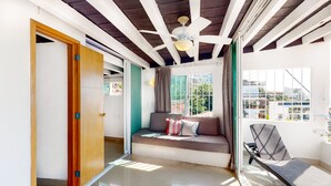 Ein modernes Wohnzimmer mit Sofa, Sessel, Deckenventilator und Blick ins Freie.