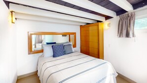 Ein Schlafzimmer mit einem Bett, einem Holzschrank, einem Spiegel und einem Fenster mit Vorhängen.