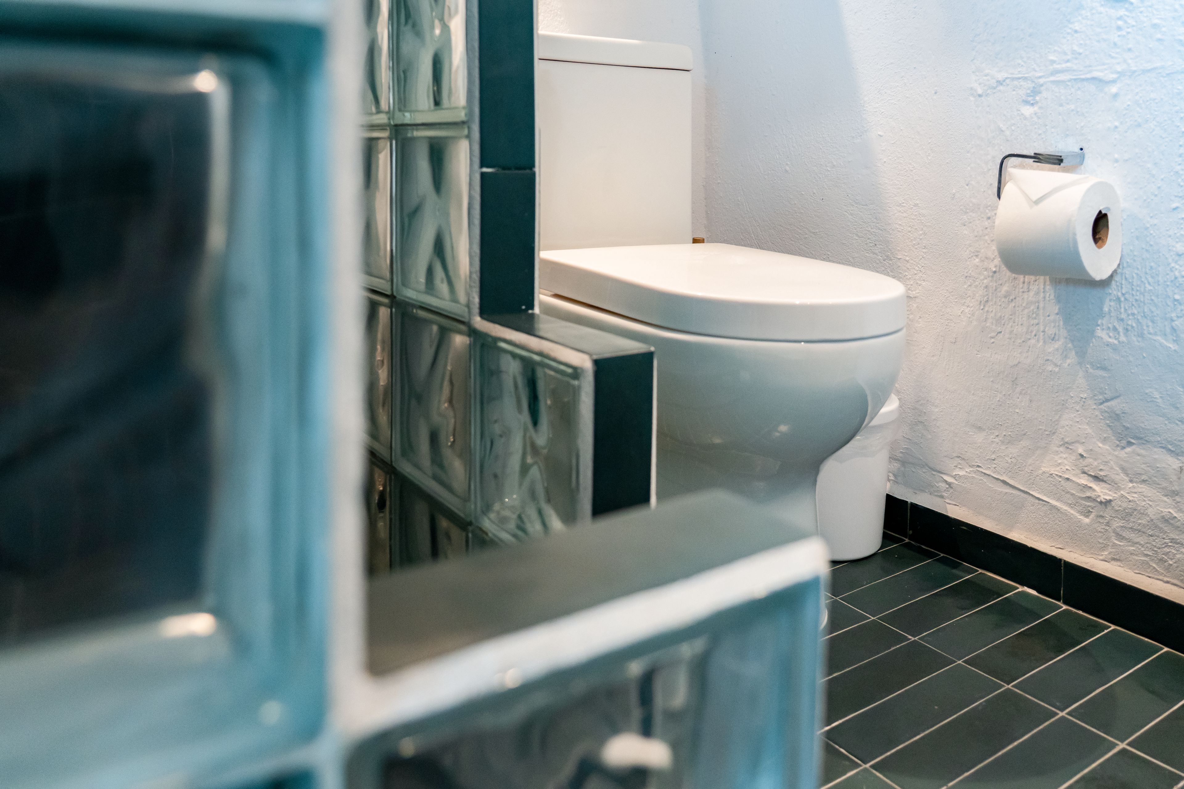A bathroom with a toilet, a wall-mounted toilet paper holder, and a tiled floor.