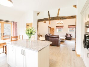 Een ruime woonkamer met keuken, houten balken, een eethoek en een centraal keukeneiland met een plant.