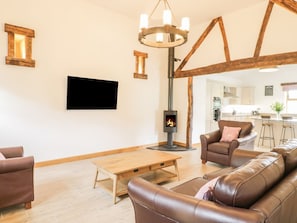 Een woonkamer met een open haard, leren banken, een houten salontafel en een aan de muur bevestigde televisie.