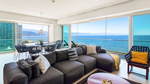 Ein modernes Wohnzimmer mit einem großen Ecksofa, einem Esstisch mit Stühlen und Blick auf das Meer.