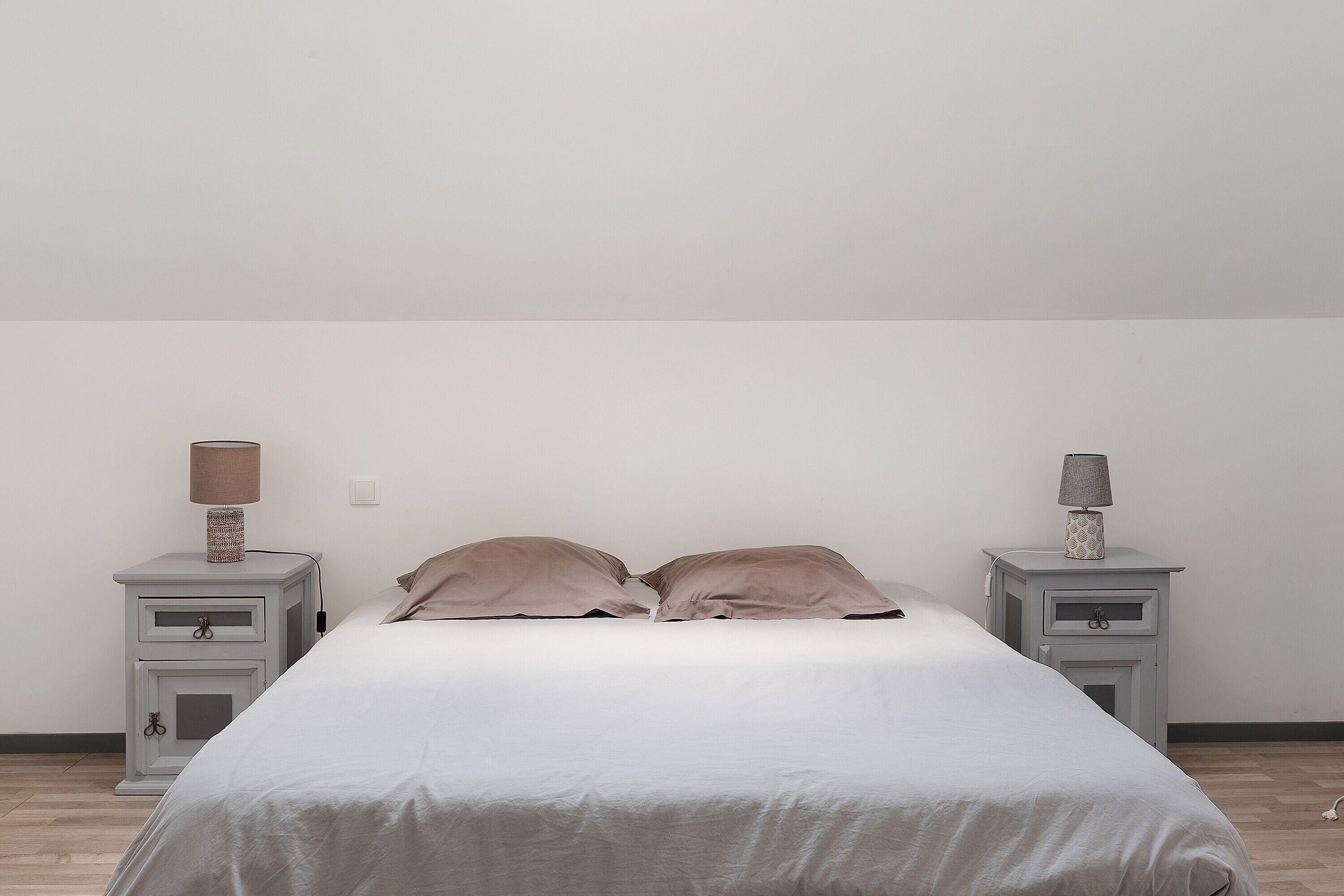 A bedroom with a bed, two bedside tables, and lamps.