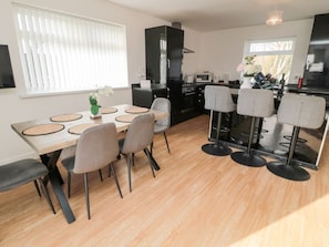 A modern kitchen with black appliances, a dining area with a wooden table and grey chairs, and a large window with blinds.