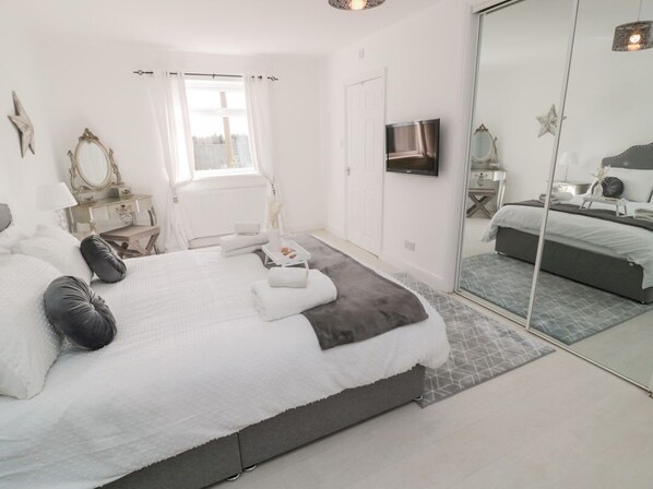 A modern bedroom with a large bed, bedside tables, a TV, and a mirror.