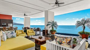 Ruime kamer met een groot bed, gele fauteuils, een houten salontafel en uitzicht op zee.