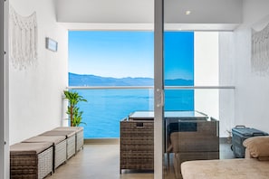 Ein Balkon mit Korbmöbeln, einem Glastisch und Blick auf das Meer.
