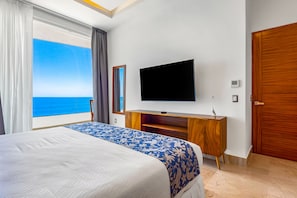 Habitación de hotel con una cama grande, televisor, cómoda de madera y vista al océano.