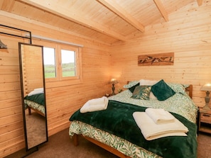 A wooden cabin bedroom with a bed, a mirror, a window, and a wall-mounted artwork.