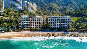 A beachfront hotel with multiple floors, a beach in the foreground, and a mountainous backdrop. - Beachfront dream retreat with pool, tennis & gym access - washer/dryer, AC (Puerto Vallarta)