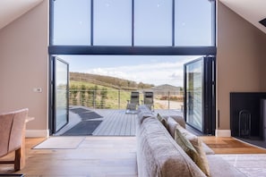 A modern interior with a large sliding glass door leading to an outdoor deck, a sofa, and a fireplace. - Hare's Hill, Thornton-Le-Dale (Pickering)