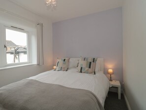 Un dormitorio con cama, mesita de noche con lámpara, ventana y vistas al exterior.