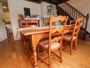 A dining table with four chairs, a staircase, and a kitchen area in the background. - Quoits Cottage, Goathland (Whitby)